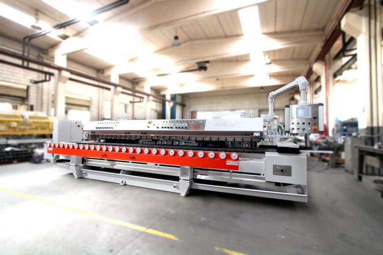 Uma máquina industrial com painéis vermelhos e brancos encontra-se numa oficina de fábrica bem iluminada, rodeada por tubagens, equipamentos e pavimentos de betão.