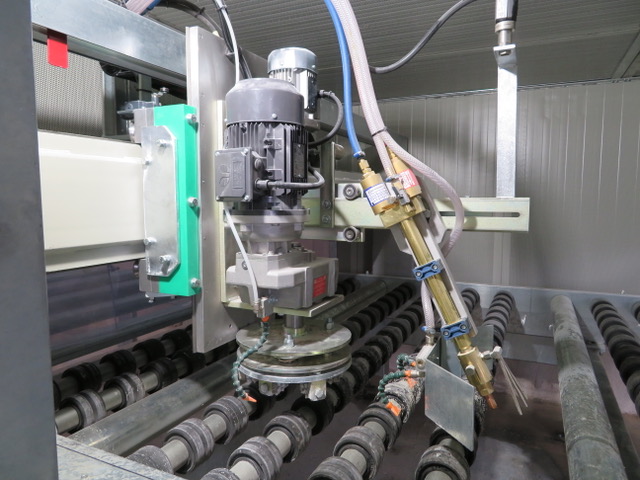 Máquina de corte industrial com cabeça de corte motorizada e mangueiras posicionadas acima de rolos metálicos numa fábrica, transmitindo precisão e automatização.