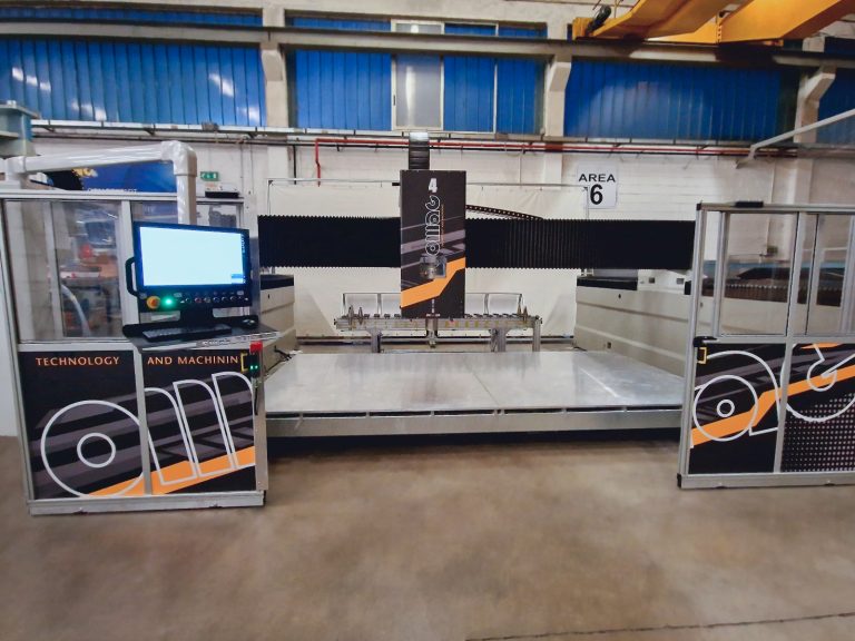 Estande de exposição de tecnologia industrial e maquinagem, com um monitor, equipamento para metalurgia e expositores nas cores laranja e preto com a indicação «Área 6».